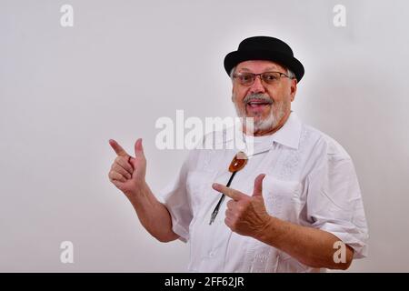 Vue d'un homme âgé portant un chapeau qui rend heureux pistolets à doigts dans l'air sur fond blanc Banque D'Images