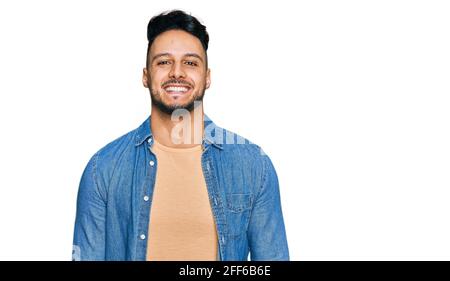 Jeune homme arabe portant des vêtements décontractés à l'air positif et heureux debout et souriant avec un sourire confiant montrant les dents Banque D'Images