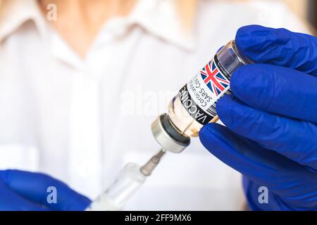 Flacon de vaccin britannique dans les mains du médecin, injection par une seringue à aiguille gros plan, vaccination et contexte du concept de santé Banque D'Images