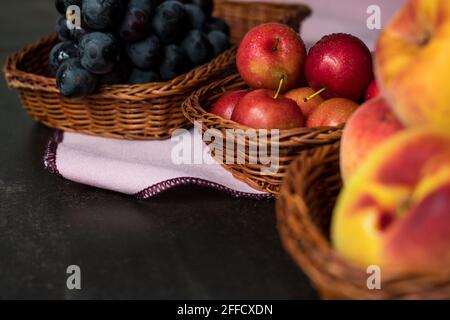 Quelques prunes, pêches et raisins dans quelques paniers sur une table noire avec un fond noir Banque D'Images