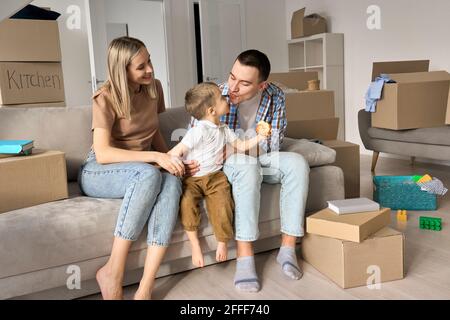 Une famille heureuse avec un enfant assis sur un canapé à la maison lors d'une journée de déménagement. Banque D'Images