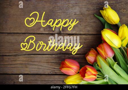 Texte joyeux anniversaire avec tulipes fraîches et colorées sur fond rustique vintage en bois. Tulipes sur panneau en bois avec texte Joyeux anniversaire.carte de vœux. Banque D'Images