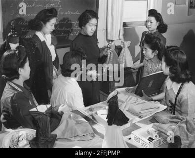 Mme Ryie Yoshizawa, enseignante de mode et de design, avec un groupe d'étudiants à table avec des équipements de tissus et de confection de vêtements, Manzanar Relocation Center, Californie, Etats-Unis, Ansel Adams, Collection Manzanar War Relocation Centre, 1943 Banque D'Images