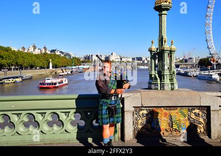 Londres, Angleterre, Royaume-Uni. Un joueur de cornemuse, équipé d'un four à écossais, joue pour les touristes sur le pont de Westminster au-dessus de la Tamise. Banque D'Images