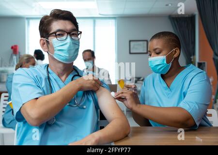 Une femme afro-américaine donne la vaccination contre le covid à un collègue mâle, tous deux dans des masques faciaux Banque D'Images