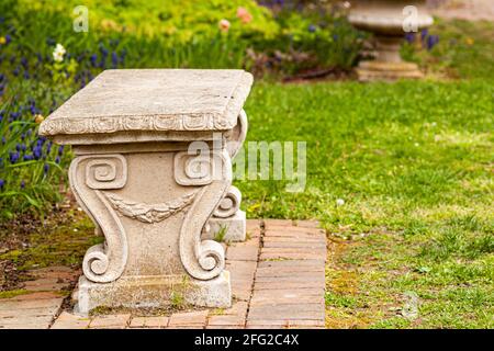 Un banc de jardin en pierre sculpté d'époque sur un terrain d'herbe dans un parc ou un jardin. Il a des motifs symétriques en spirale rappelant les figues grecques ou romaines anciennes Banque D'Images