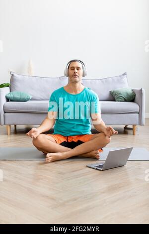 Photo d'un homme médite à la maison - en utilisant de l'Internet pour surveiller l'entraînement. Il écoute de la musique relaxante de méditation à travers des écouteurs. Domicile Banque D'Images