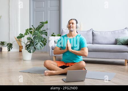 Photo d'un homme méditant à la maison - utilisant de l'Internet pour surveiller l'entraînement. Il écoute de la musique relaxante de méditation à travers des écouteurs. Accueil W Banque D'Images