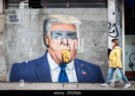 Porto, Portugal. 24 avril 2021. Une femme portant un masque porte un bébé alors qu'elle passe devant un graffiti de l'artiste portugais kilo. Le graffiti est un point de vue satirique qui mélange Donald Trump et la banane collée au mur avec des œuvres d'art sur ruban adhésif. Le Portugal est à la 3ème étape du plan de déconditionnement mais les magasins, les restaurants et les cafés sont toujours fermés le week-end durant l'après-midi. Crédit : SOPA Images Limited/Alamy Live News Banque D'Images