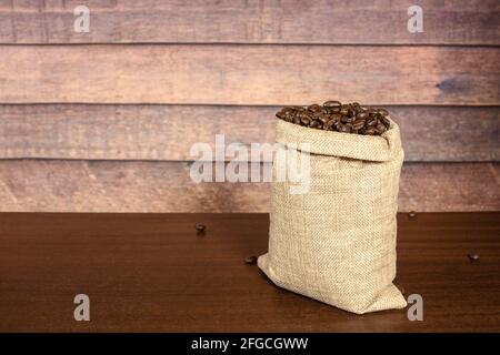 Grains de café. Grains de café torréfiés durs dans un sac jute en toile de jute, sur une table en bois marron avec un fond rustique. Banque D'Images