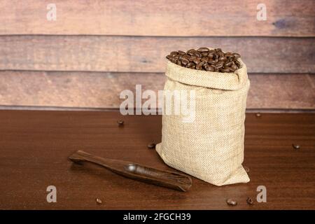 Grains de café. Grains de café torréfiés durs dans un sac de jute et une spatule à café, sur une table en bois marron avec un fond rustique. Banque D'Images