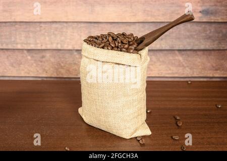 Grains de café. Grains de café torréfiés durs dans un sac jute à bavette avec spatule à café, sur la table en bois brun avec fond rustique. Banque D'Images