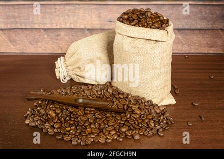 Grains de café. Grains de café torréfiés dans deux sacs de jute et beaucoup de café dispersé avec une spatule, sur la table en bois brun avec du backgroun rustique Banque D'Images