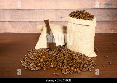 Grains de café. Grains de café torréfiés dans deux sacs de jute et beaucoup de café dispersé avec la spatule, sur la table en bois brun avec le backg rustique Banque D'Images