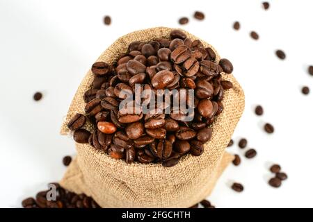 Grains de café. Sac de jute avec grains de café torréfiés et quelques grains de café. Isolé sur fond blanc. Banque D'Images