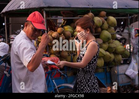 Livraison de noix de coco, femme cambodgienne portant un masque de protection et utilisant un smartphone au marché de Kandal pendant la pandémie du coronavirus. Phnom Penh, Cambodge. 18 mars 2020. © Kraig Lieb Banque D'Images