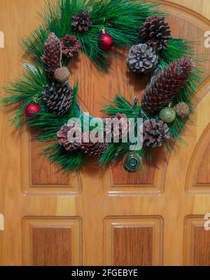 Vue de face d'une couronne de Noël traditionnelle composée de branches à feuilles persistantes, de feuilles de houx et de baies suspendues à la porte d'entrée Banque D'Images