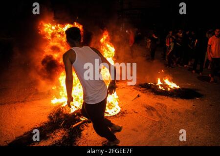 Gaza, Palestine. 24 avril 2021. Les Palestiniens brûlent la roue et lèvent le drapeau palestinien lors d'une manifestation à l'ouest de la ville de Gaza en faveur des Palestiniens de Jérusalem-est. Depuis le début du ramadan, le 13 avril, les tensions se sont élevées à Jérusalem-est, dans un premier temps à la suite de l'interdiction par les autorités israéliennes de se réunir autour de la porte de Damas de la vieille ville, où les Palestiniens ont tendance à se réunir dans la soirée pendant le ramadan. Les tensions se sont encore exacerbées jeudi soir, lorsque les extrémistes juifs ont défilé près de la vieille ville de Jérusalem-est pour crier « mort aux Arabes Banque D'Images