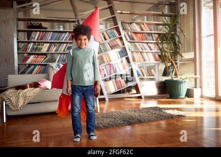 Un petit garçon avec un jouet de fusée sur son dos pose dans une atmosphère détendue à la maison. Maison, jeu, enfance Banque D'Images