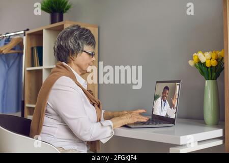 Femme âgée ayant consultation en ligne médecin sur ordinateur portable assis à accueil Banque D'Images