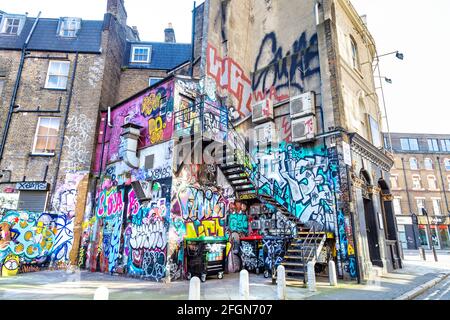 Arrière d'un bâtiment couvert de graffiti, art de rue, étiquettes et peintures murales sur New Inn Yard, Shoreditch, Londres, Royaume-Uni Banque D'Images