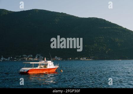 Un bateau à moteur rouge avec un auvent du soleil près de la côte de la ville de Perast flotte sur l'eau. Banque D'Images