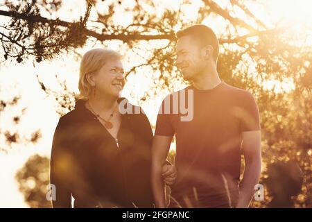 Mère marchant avec son fils à la lumière dorée du soleil. Femme âgée et jeune homme adulte parlant dans un parc public. Banque D'Images