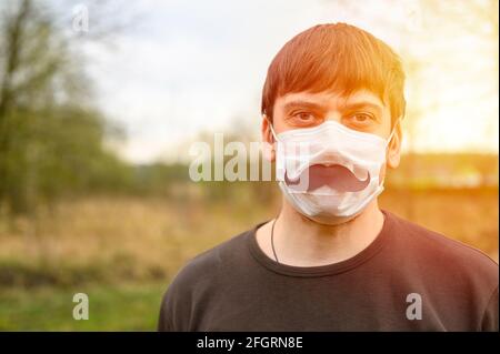 la journée des pères au cours du concept de quarantaine covid-19. portrait d'un jeune homme européen dans un masque de protection et une moustache en papier sur le fond de Banque D'Images