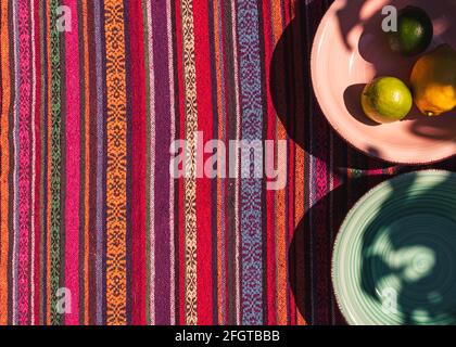 image d'assiettes à soupe rose et vert pastel, de deux citrons et de citron vert sur une nappe colorée prise au soleil Banque D'Images