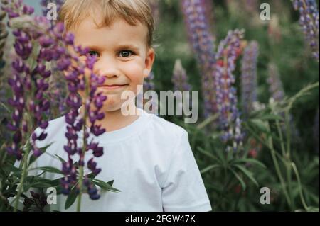 portrait d'un adorable petit garçon de quatre ans heureux garçon aux fleurs lupins de fleur dans un champ de nature extérieur Banque D'Images