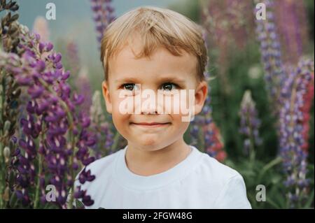 portrait d'un adorable petit garçon de quatre ans heureux garçon aux fleurs lupins de fleur dans un champ de nature extérieur Banque D'Images