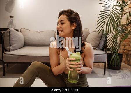 La femme fait de l'exercice à la maison. Jeune femme modèle va pour le sport dans l'appartement, elle tient un shaker de protéines avec le lait dans ses mains. Banque D'Images