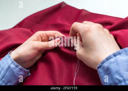 La couturière rade les vêtements à la main. Les mains de la femme se rapprochent. Banque D'Images