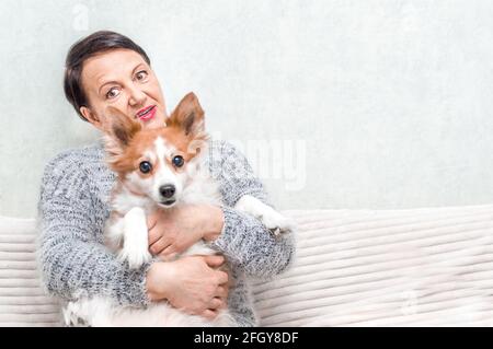 Portrait d'une femme âgée jouant avec son chien sur un canapé Banque D'Images