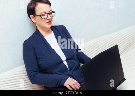Portrait d'une femme âgée, ordinateur portable, assis sur un canapé Banque D'Images