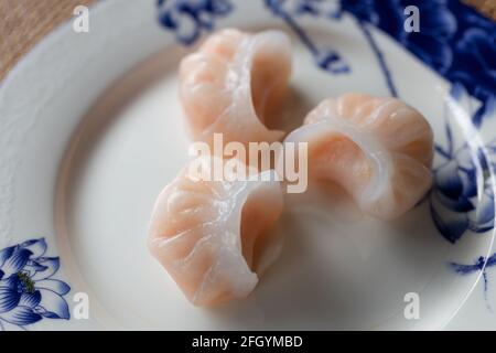 Plat traditionnel chinois authentique : boulettes de style cantonais Har gow aux crevettes, gros plan sur une assiette blanche et bleue Banque D'Images