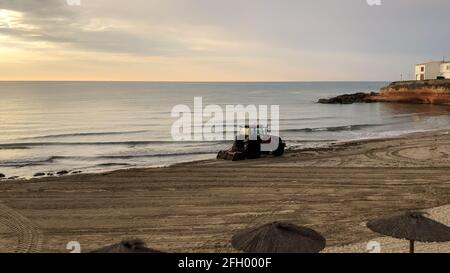 Alicante, Espagne - Alicante, 2021: Tracteur nettoyant la plage de la mer des algues au lever du soleil tôt le matin Banque D'Images