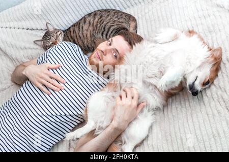 Portrait d'un jeune homme allongé avec son chien et chat sur le lit Banque D'Images