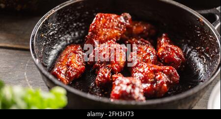 Ailes de poulet marinées épicées dans une casserole sombre. Banque D'Images