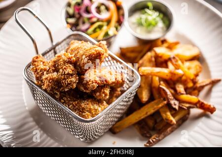 Nuggets de poulet frits dans un panier métallique servi avec des frites sur une assiette blanche. Banque D'Images