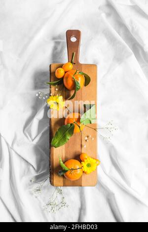 Vue de dessus des mandarines mûres avec des cumquats et des fleurs de jaune Chrysanthèmes sur planche à découper sur fond blanc Banque D'Images
