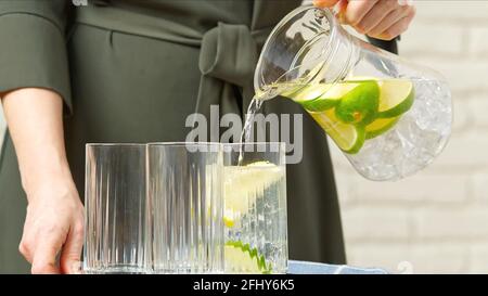 Buvez de l'eau. Main de femme versant de l'eau pure fraîche avec des morceaux de citron du pichet dans le verre dans le concept de santé et de régime du matin. Une vie saine Banque D'Images