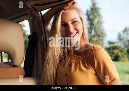 Belle femme blonde vêtue de vêtements décontractés penchée sur une camionnette de camping Banque D'Images