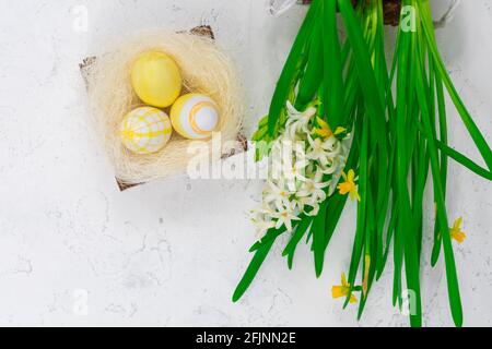 Concept de Pâques. Oeufs de Pâques jaunes dans un nid à côté d'un bouquet de jonquilles sur une table en béton blanc. Vue de dessus. Place pour une inscription. Banque D'Images