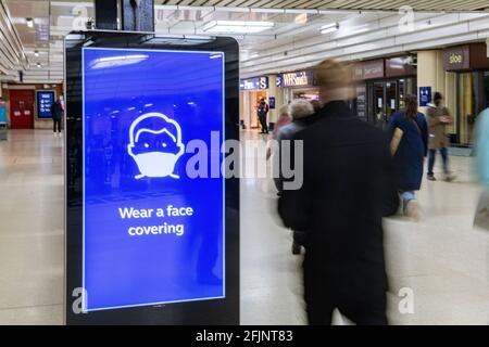 Des passagers flous marchent devant un avis de porter une couverture faciale pendant la pandémie du coronavirus en 2021 à la gare Victoria, à Londres Banque D'Images