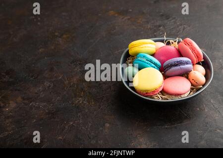 Macarons multicolores et œufs au chocolat dans un bol en céramique sur fond de béton noir. Vue latérale, espace copie, encore la vie. Petit déjeuner, matin, concept Banque D'Images