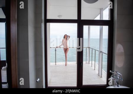 Belle jeune femme aux cheveux bouclés repose sur une terrasse ouverte donnant sur la mer bleue. Une fille dans un body beige, avec des jambes longues et bien entretenues Banque D'Images