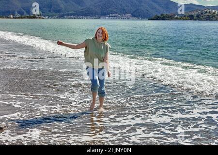 Une jeune femme marche pieds nus sur la plage dans la zone de surf. Banque D'Images