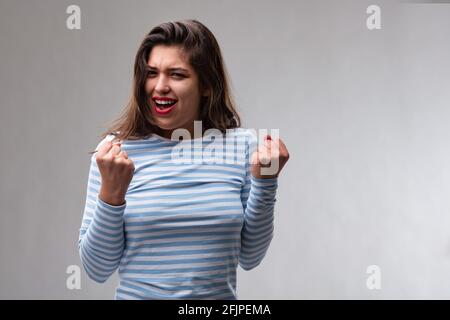 Jeune femme exubérante qui applaudit son succès ou montre la motivation poinçante l'air avec ses poings et la voix dans un studio portrait Banque D'Images