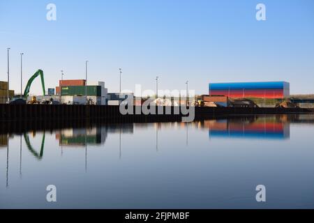 Wustermark, Allemagne. 21 avril 2021. Les véhicules de construction et les conteneurs du HavelPort se reflètent dans l'eau du Havelkanal. Le port intérieur, fondé en 2013, est situé au centre de distribution des marchandises (GVZ) et offre de l'espace pour trois navires en même temps que son quai de 400 mètres de long. La façade de couleur arc-en-ciel dissimule le centre de distribution de la chaîne dm. Tous les magasins dm de l'est de l'Allemagne sont fournis avec des marchandises d'ici. Credit: Soeren Stache/dpa-Zentralbild/dpa/Alay Live News Banque D'Images